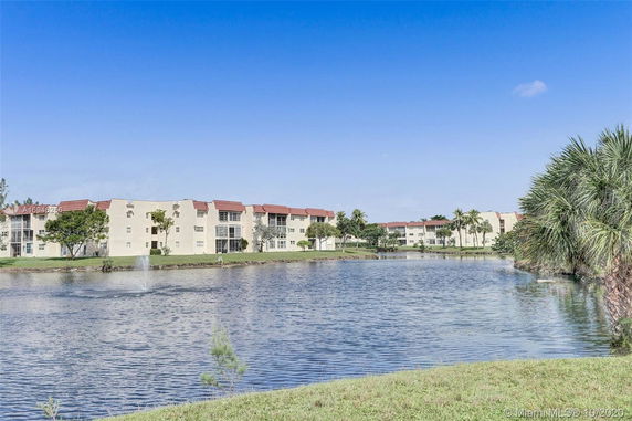 Row of residential buildings with red roofs seen from across a pond with a fountain.