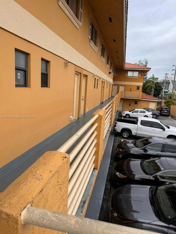 Outdoor parking area with multiple vehicles adjacent to a two-story building.