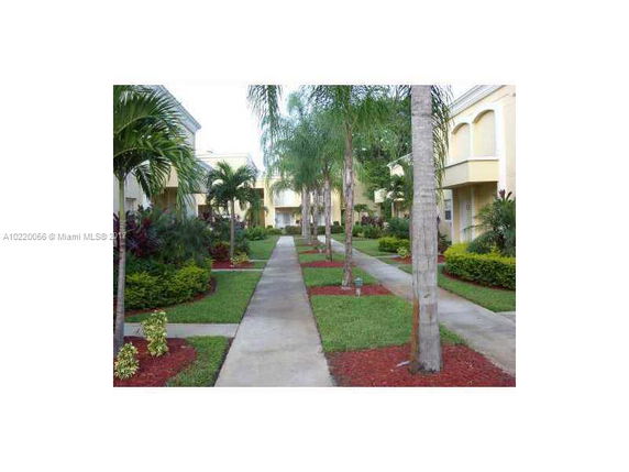 Front view of a two-story apartment complex with landscaped pathways and palm trees.