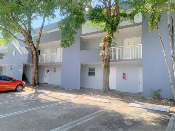Outdoor parking area in front of a two-story apartment building featuring balconies and staircases.