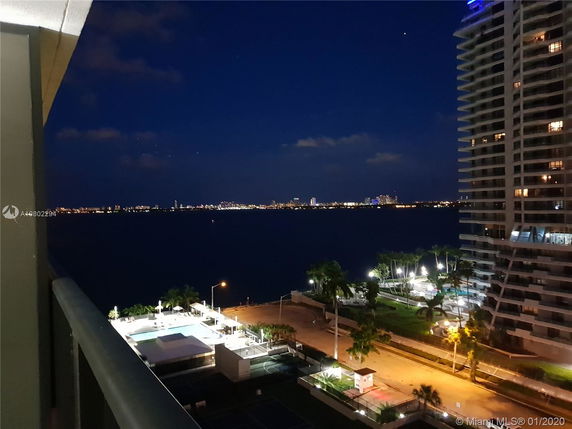 Nighttime view of cityscape from a high vantage point with a tall building and water in the distance.