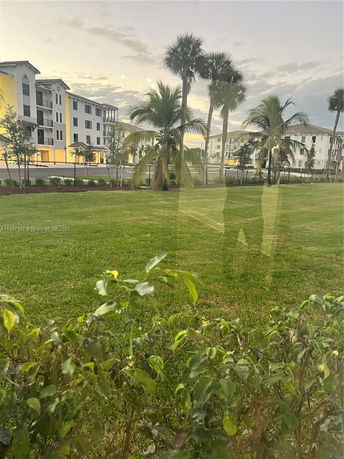View of apartment buildings with green lawn and palm trees.