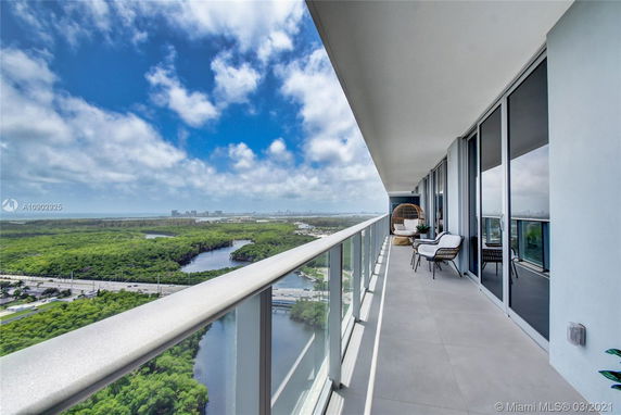 Wide balcony view from a high-rise building with distant cityscape and lush greenery.