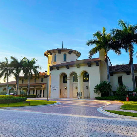 Front view of a large, elegant building with arched windows and a prominent tower, surrounded by palm trees.