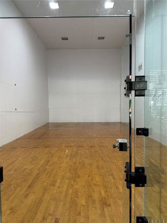 Indoor squash or racquetball court with wooden flooring and glass door.