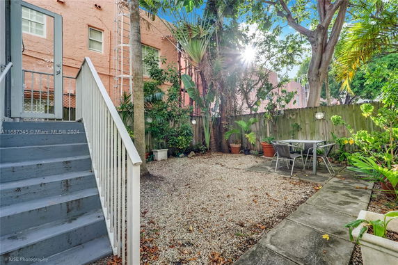 Backyard view with stairs leading down to a gravel area, outdoor furniture, and surrounding trees and plants.