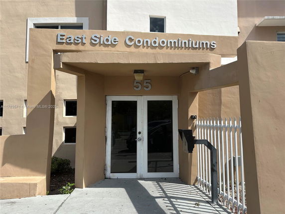 Front view of a beige condominium entrance with a sign reading 'East Side Condominiums' and the number 55.