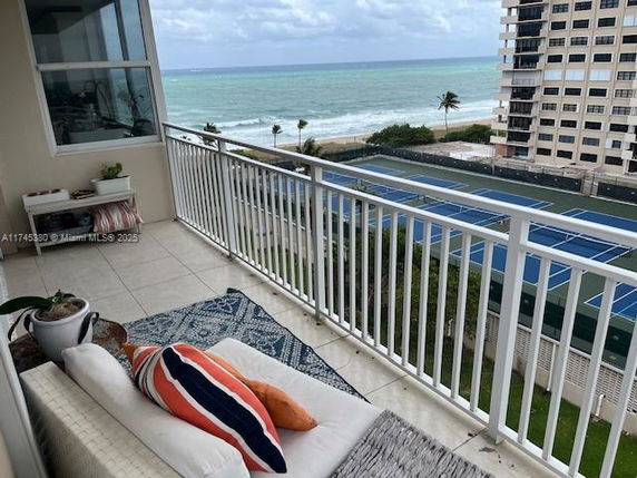 Balcony view overlooking tennis courts and the ocean, with adjacent building.