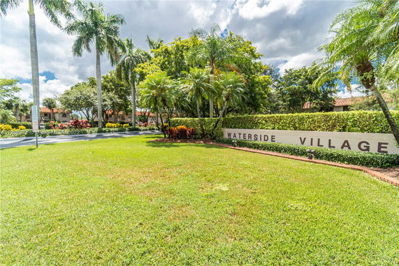 View of a landscaped area with palm trees and a sign that reads 'Waterside Village'.