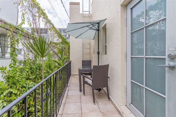 Narrow balcony with a table, chairs, umbrella, and surrounding plants.