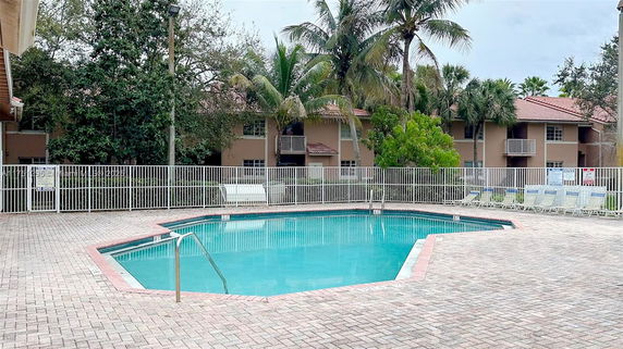 Outdoor swimming pool area with surrounding buildings and palm trees.