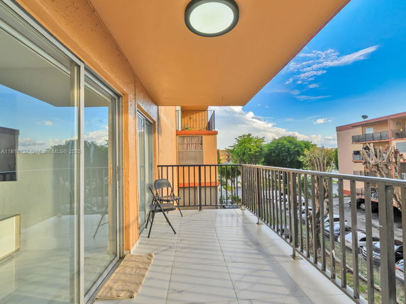 Balcony view with sliding glass doors and railing overlooking adjacent buildings and trees.