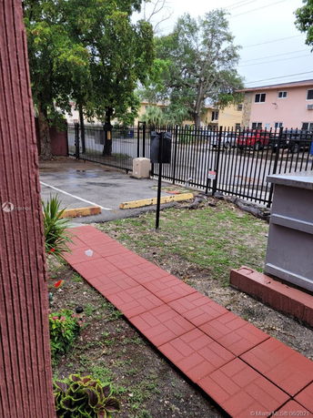 Outdoor parking area with a paved walkway and metal fence.