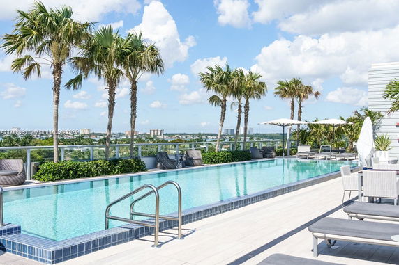 Outdoor swimming pool with lounge chairs and palm trees on a rooftop.