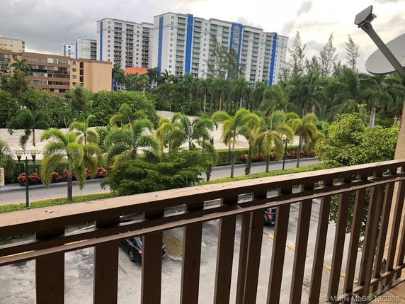 View from a balcony showing tall buildings and lush palm trees.