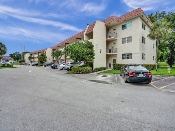Outdoor parking area in front of a multi-story residential building with palm trees.