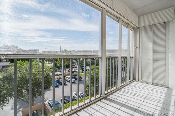 View from a balcony with railings, overlooking a parking lot with cars and trees.