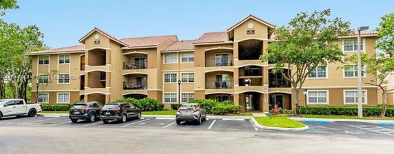 Front view of a multi-story apartment building with balconies and parking area in front.