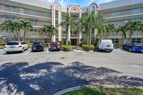 Front view of a multi-story apartment building with balconies and a parking area in front.