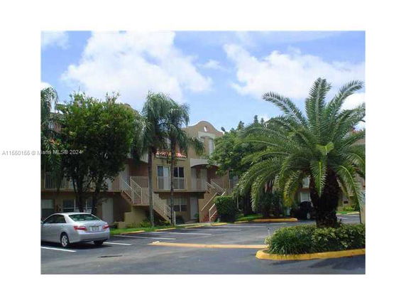 Front view of a two-story apartment building with exterior staircases and palm trees.