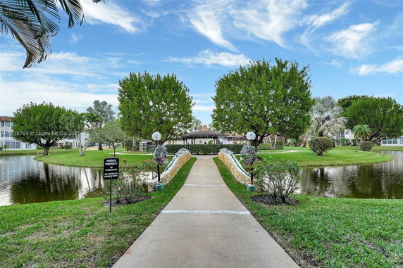 View of a landscaped area with a walkway, trees, and water features leading to a distant building.