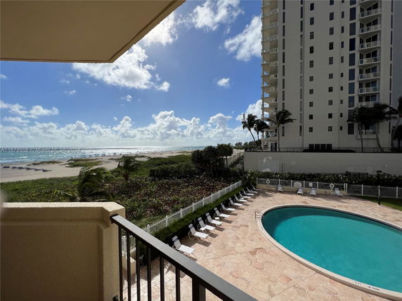 View from a building overlooking a pool and beach with a high-rise building nearby.
