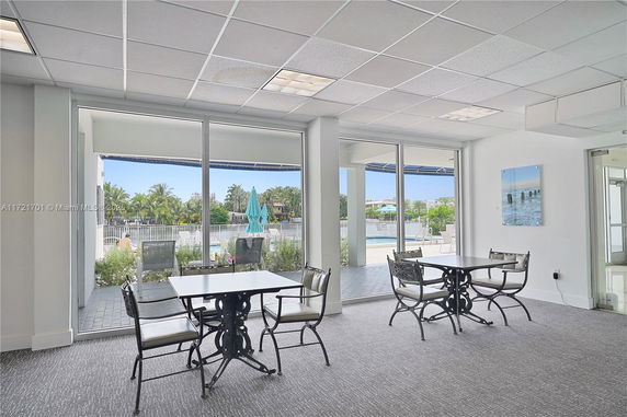 Indoor seating area with tables and chairs overlooking a swimming pool through large glass windows.