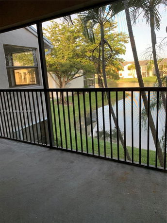 View from a screened balcony showing nearby buildings and a pond.