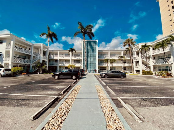 Front view of a multi-story apartment building with a blue decorative wall and parking area.