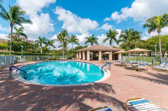 Outdoor swimming pool area with surrounding lounge chairs and a small building nearby.
