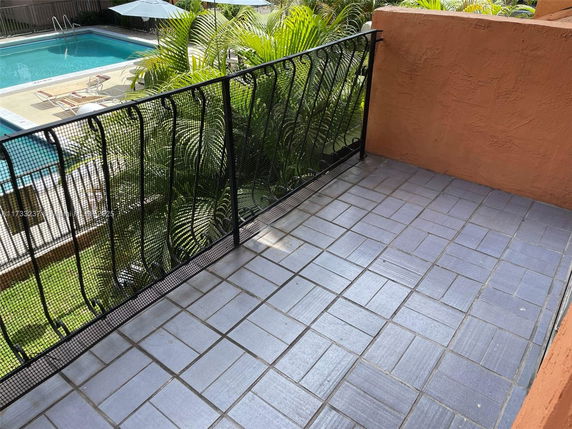 View of a tiled balcony with a railing overlooking a swimming pool.