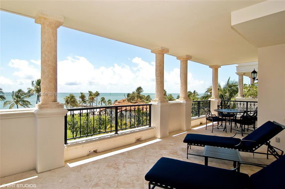 Panoramic view from a balcony with ocean in the background and palm trees below.