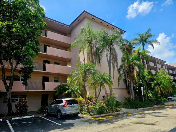 Front view of a multi-story apartment building with balconies and surrounding palm trees.