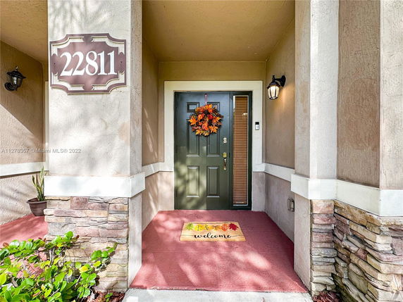 Front view of a house entrance with a welcome mat and decorative wreath on door.
