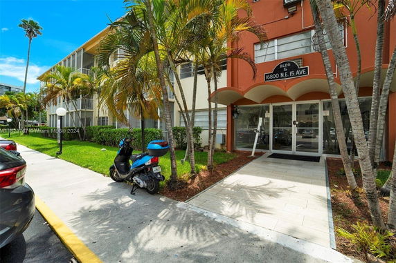 Front view of a multi-story residential building with a glass entrance and surrounding palm trees.