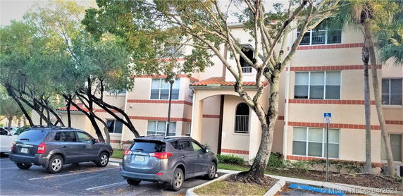 Exterior view of a multi-story residential building with a parking area in front.
