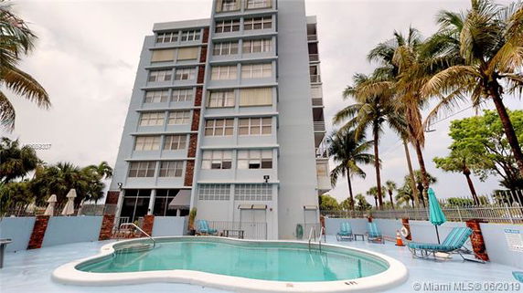 Front view of a multi-story building with a swimming pool area in the foreground.