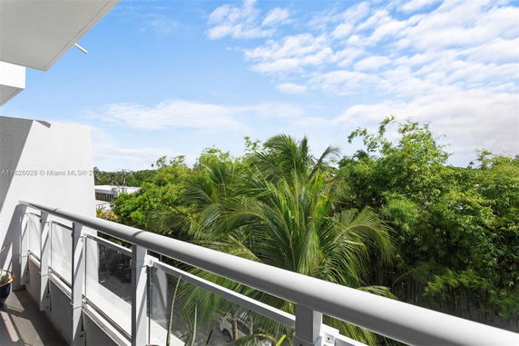 View from a building balcony overlooking lush green trees and a clear blue sky.
