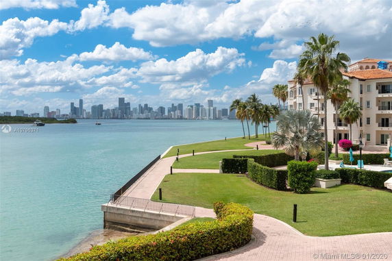 View of a multi-story building near a waterfront with a city skyline in the distance.