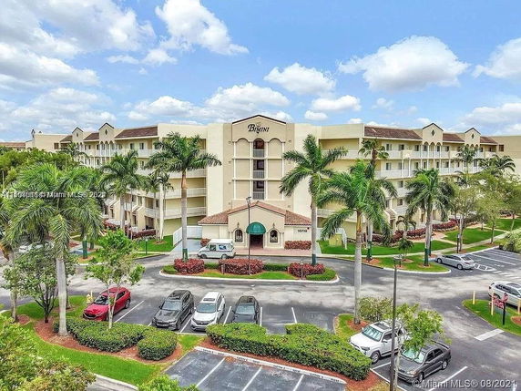 Front view of a multi-story residential building with palm trees and a parking area in front.