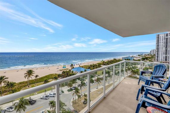 View from a building balcony overlooking a sandy beach and ocean.