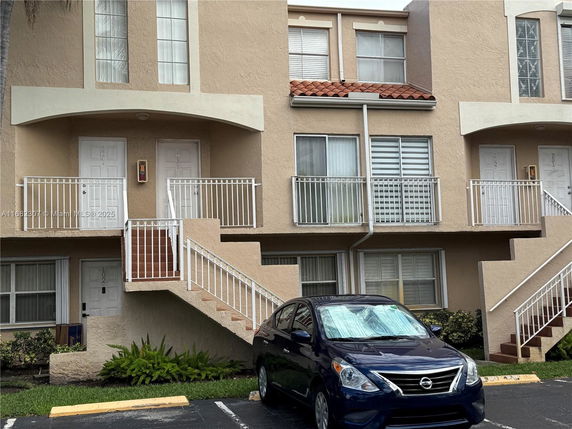 Front view of a multi-story apartment building with exterior staircases and a car parked in front.