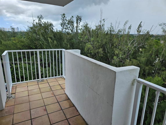View from a balcony with a railing overlooking greenery and distant buildings.