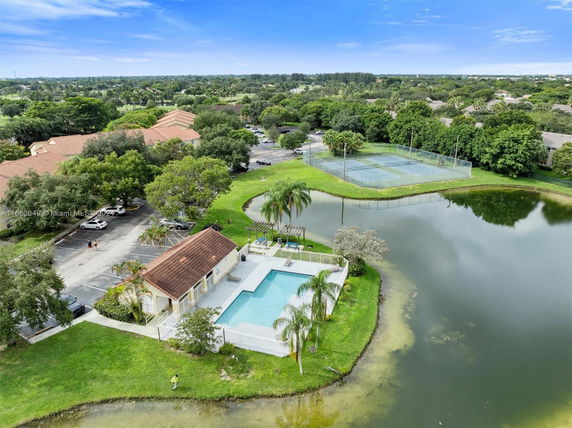 Aerial view of a swimming pool area, tennis courts, and a landscaped environment with buildings in the background.