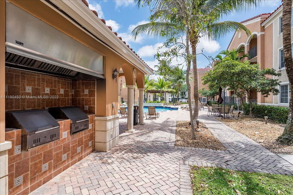 Outdoor area with brick grills and swimming pool surrounded by palm trees and seating.