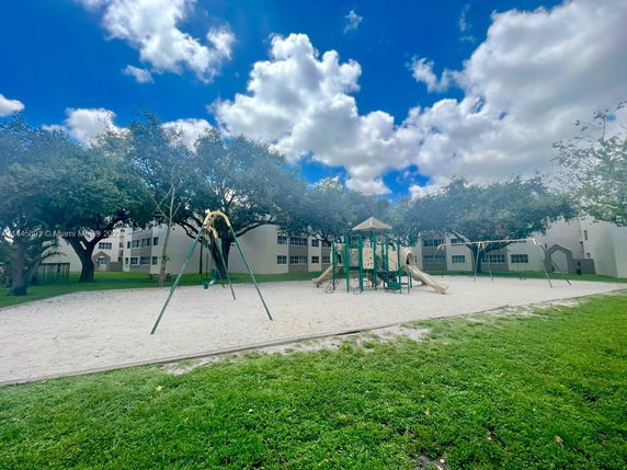 Outdoor playground with swings and slides surrounded by trees and buildings.