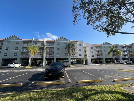 Front view of a multi-story apartment building with parking spaces in the foreground.