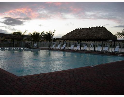 Outdoor swimming pool with lounge chairs and a thatched roof structure nearby.