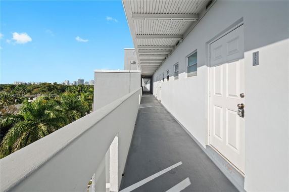 Exterior corridor of a building with doors leading to apartments and view of surrounding greenery and distant buildings.