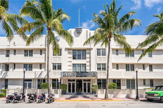 Front view of a multi-story building with palm trees and motorbikes in front.